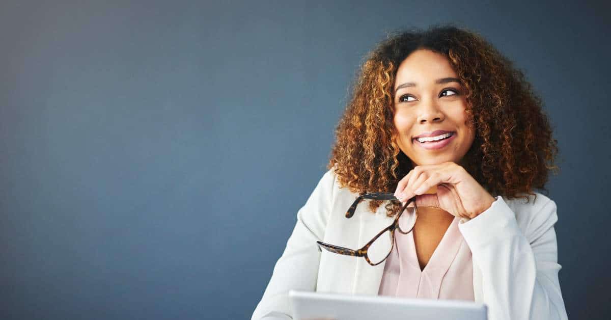 Woman holding glasses, resting her chin on her fist, thinking, with a smile on her face