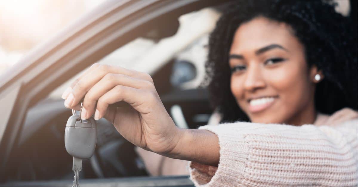 Picture of a young woman in the driver's seat holding a car key.