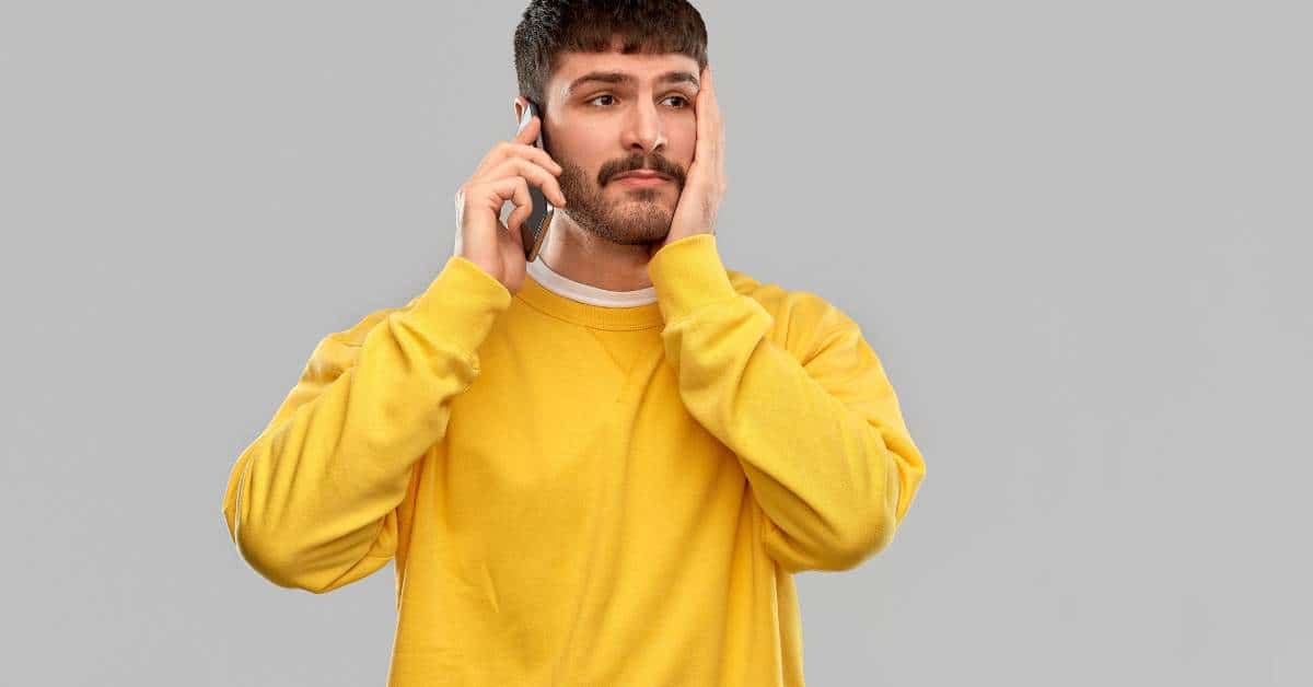 Male college student holding a cell phone to his ear and his hand on his cheek.