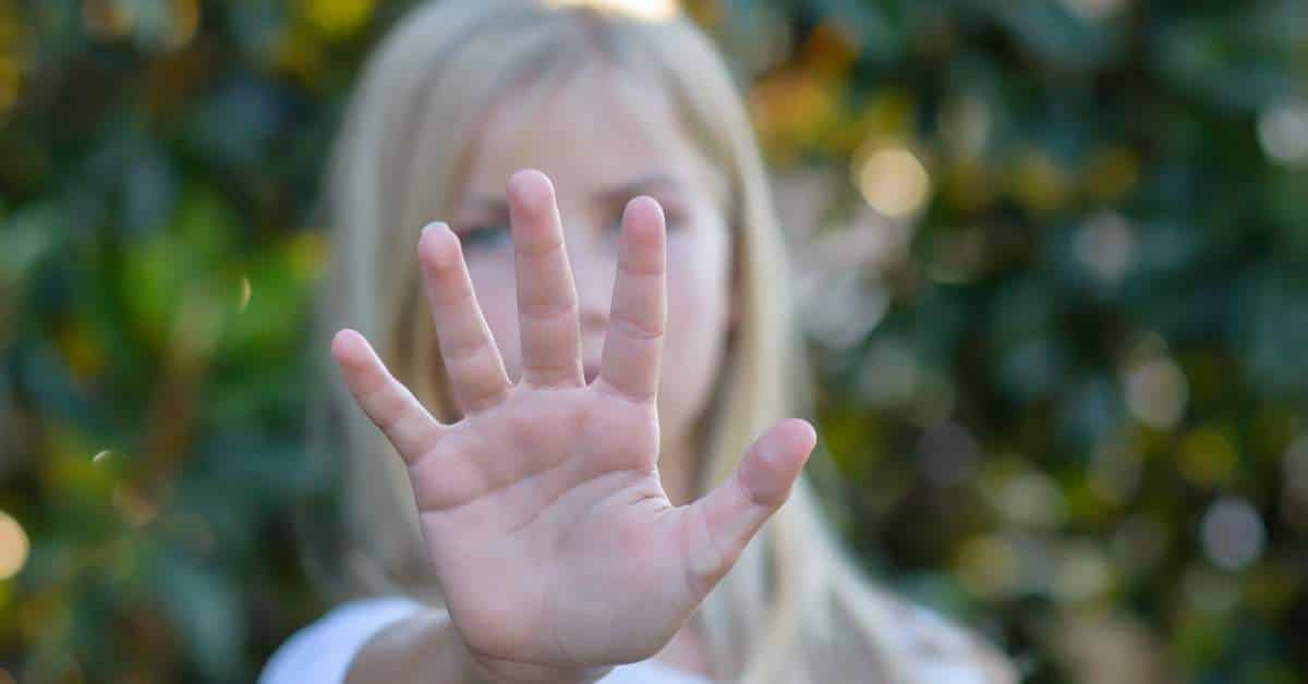 Blond teen girl holding her hand in front of her to push someone away.