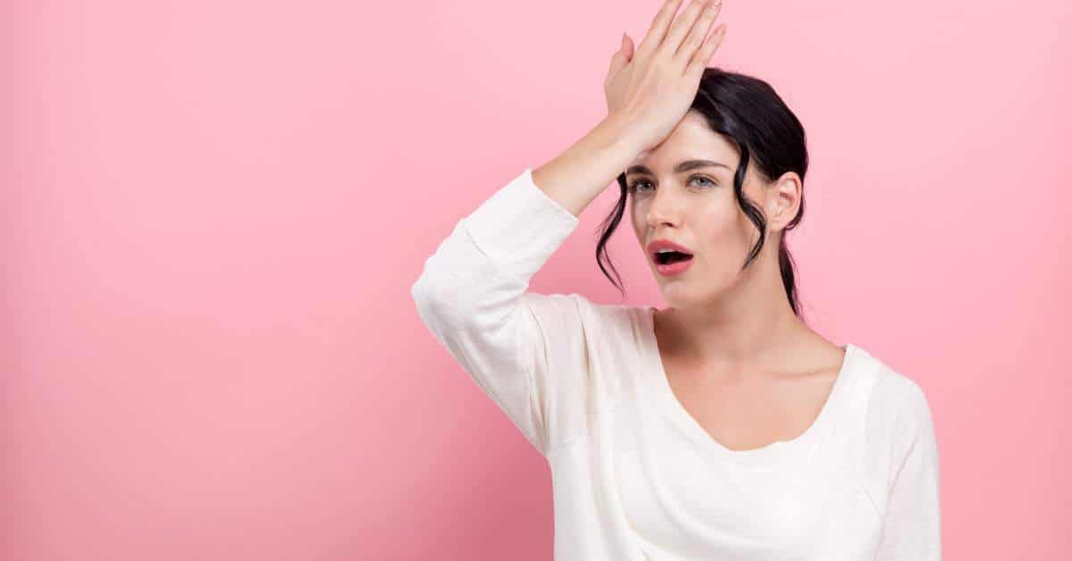 Woman holding her hand to her head with a surprised expression on her face.