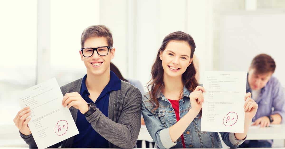 Smiling teen boy and girl each holding up a graded paper and smiling.