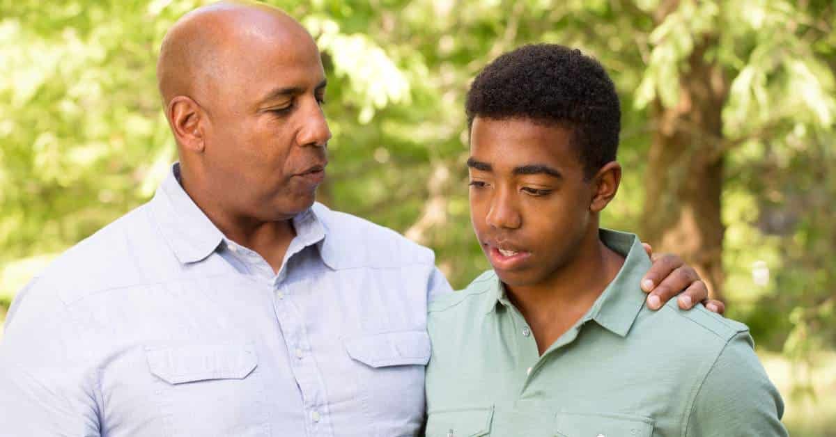 Father with his arm around his teen son's shoulder. They are having a serious conversation.