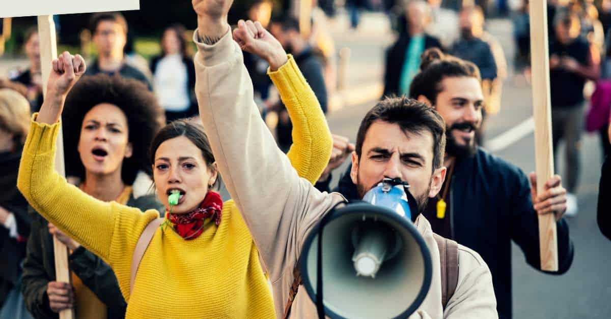 Students raising their arms with a student in the forefront lifting a megaphone as they protest.