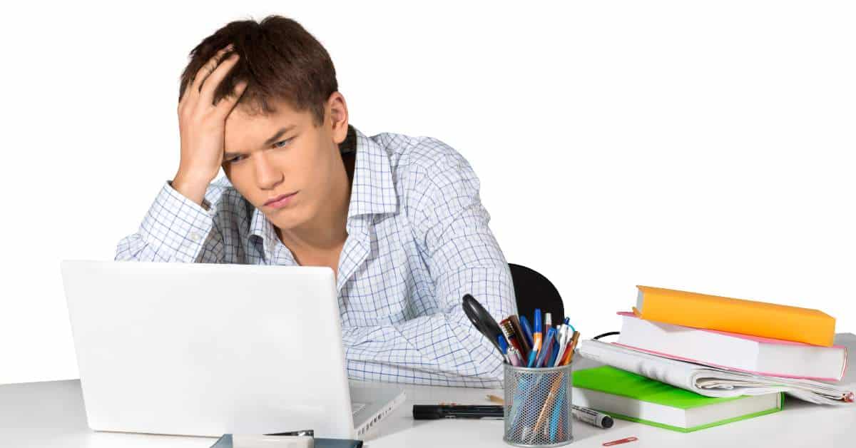 Teen slumped in front of a laptop computer with his hand in his hair looking frustrated.