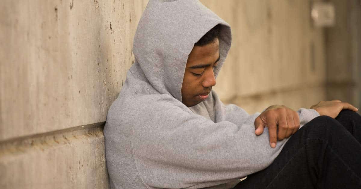 Unhappy teen wearing a gray hoodie with his back agains a wall.