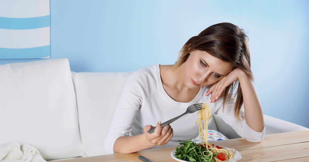 A teen girl with her head resting on ther hand looking dejectedly at a plate of food.