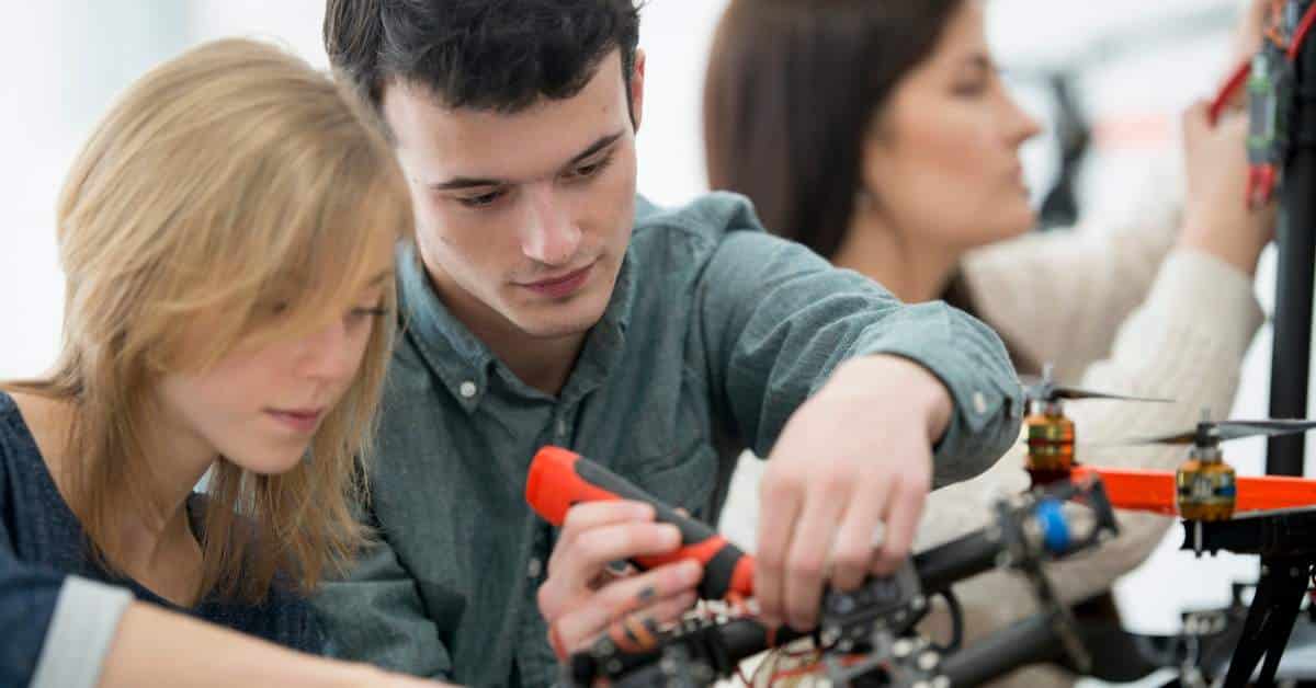 Young man and woman working on an engineering project. He is holding a screw driver and screwing something in
