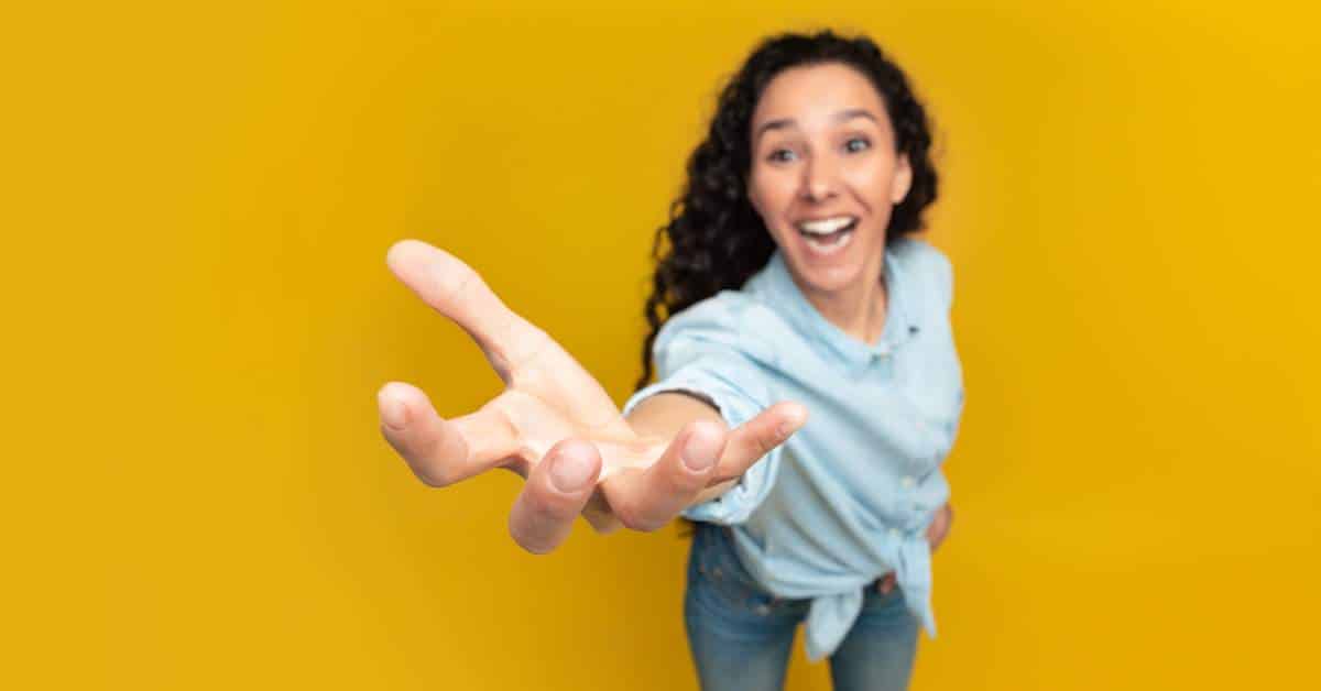 Young woman standing against a yellow backdrop holding out her hand as she reaches forward.