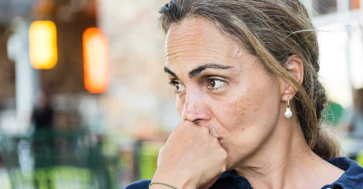 Concerned, middle aged woman holding her fist up to her mouth and looking off to the side.
