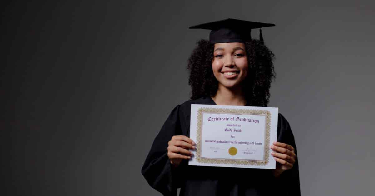 African American woman in a black cap and gown holding a certificate of graduation and smiling.