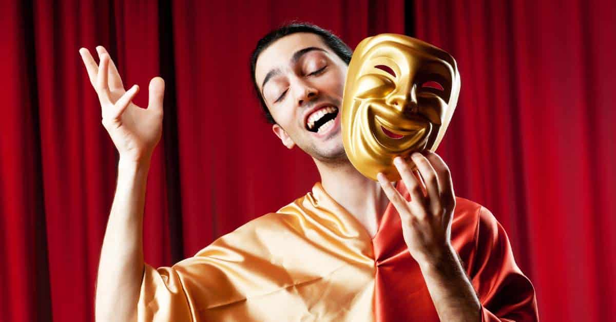 Young man acting on the stage and removing a gold acting mask from his face