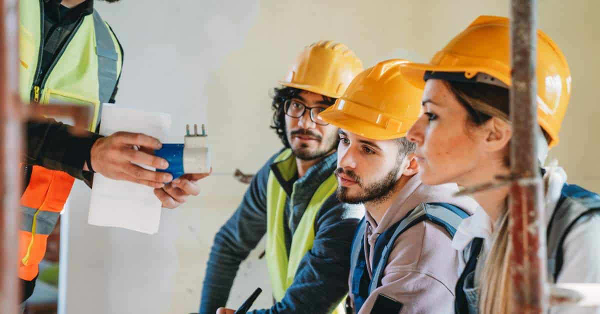 Three students with hard hats on look up a teacher