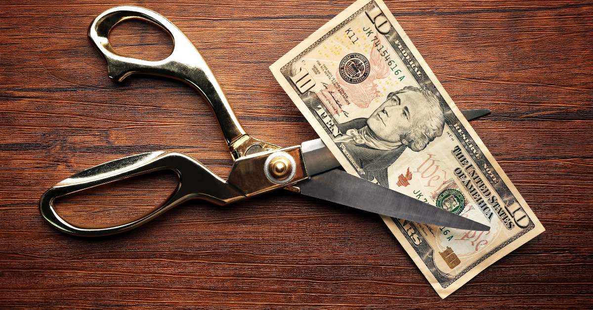 A $10 bill with large silver scissors about to cut it