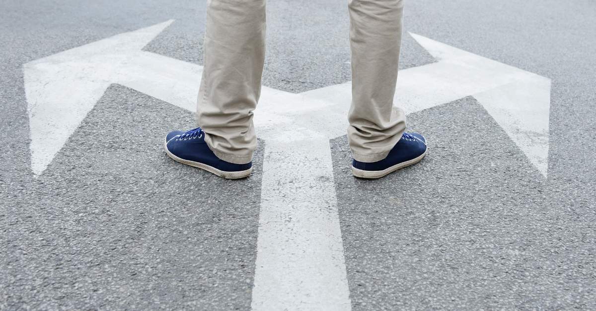 Person standing on pavement with two areas going opposite directions