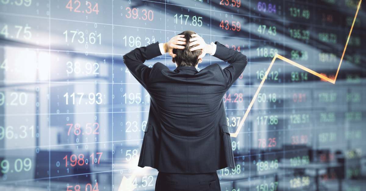 Man with his back to the camera, hands on his head in distress, looking at stock market tickers.